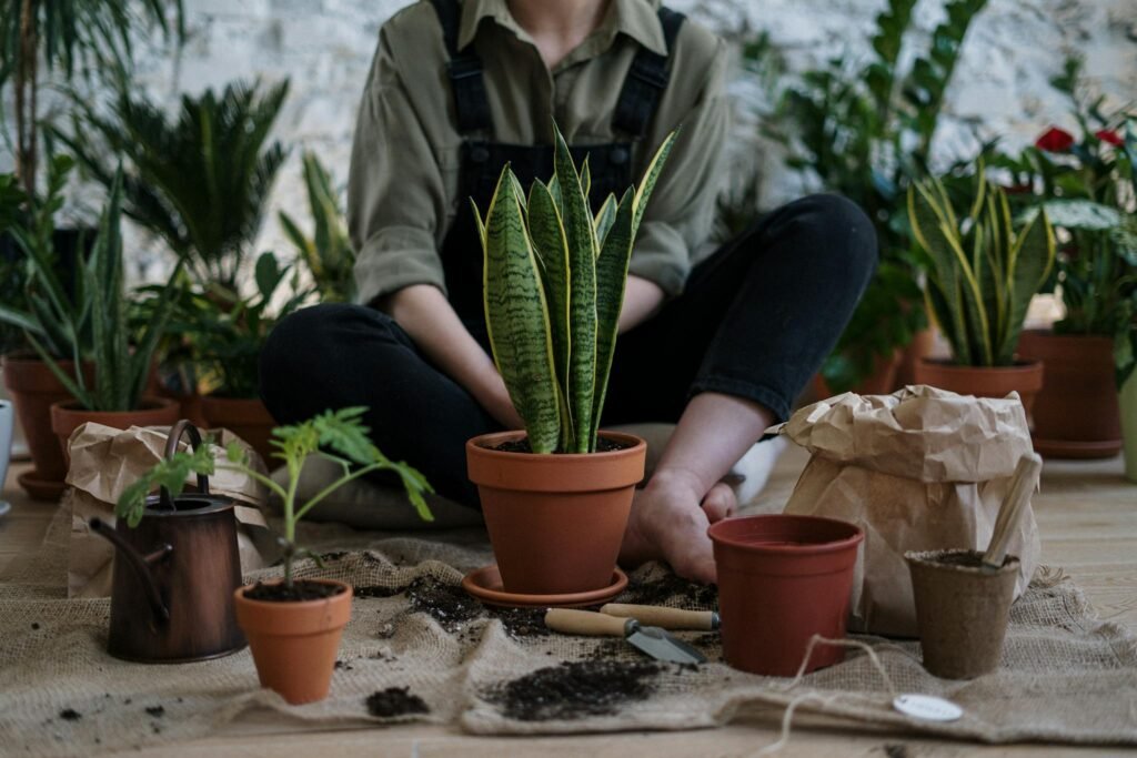 Person sitting indoors surrounded by potted plants and gardening tools, fostering nature